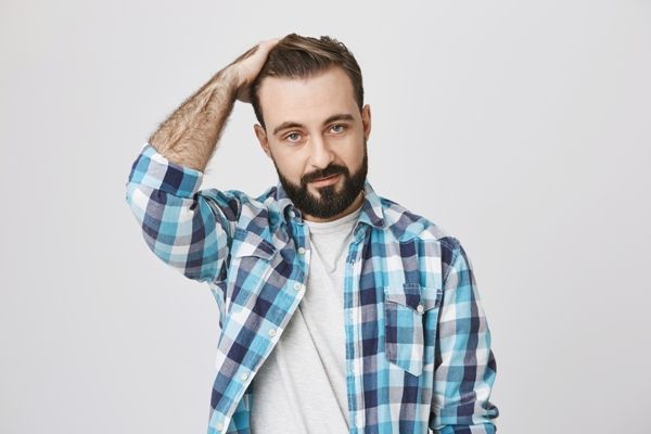 hombre blanco con camiseta blanca y camisa a cuadros luciendo los resultados del tratamiento de cabello