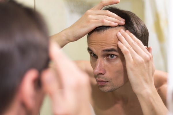 Dormir después del injerto de cabello - Joven de ojos verdes mira con detenimiento el avance de sus entradas frente al espejo