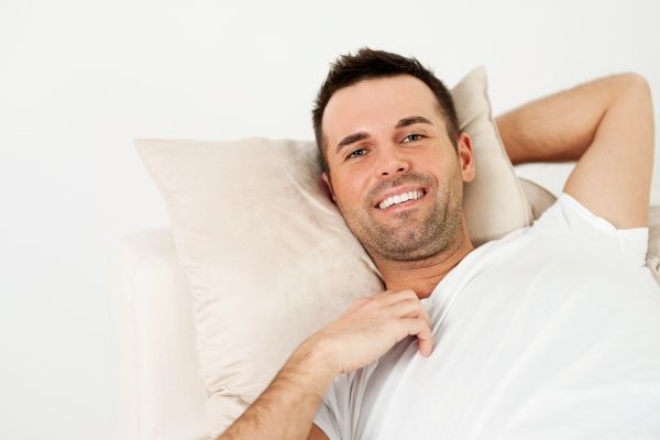Dormir después del injerto de cabello - Hombre sonriente toma una almohada para descansar plácidamente tras una cirugía