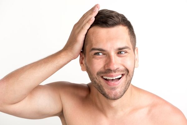 hombre joven muy contento pasándose la mano por su cabello implantado, muy alegre con los resultados del implante capilar