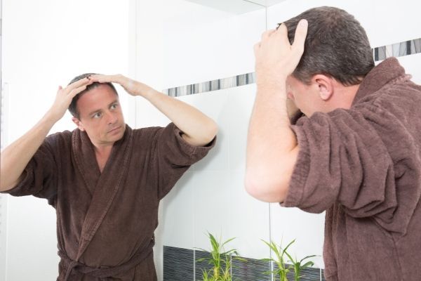 Injerto de cabello 10 años después - hombre adulto en albornoz tras la ducha comprobando el retroceso de la línea del cabello