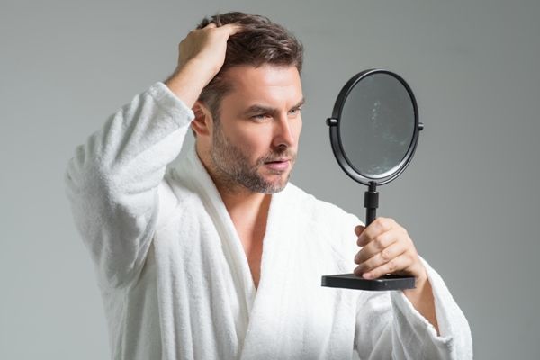 tratamiento para la hidratación del pelo - hombre en albornoz revisando su cabello delante del espejo