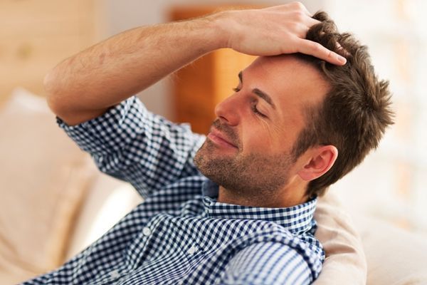 hidratar el pelo en casa - hombre recostado en el sofá con una camisa de cuadros, pasando la mano por su cabeza con cara de felicidad