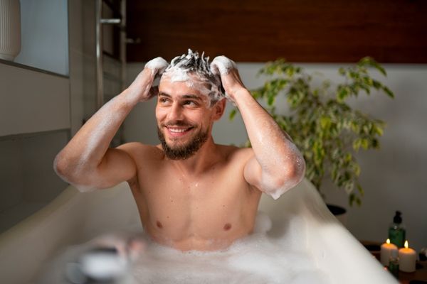 hombre sonriente en la bañera enjabonando su cabello para lavarlo