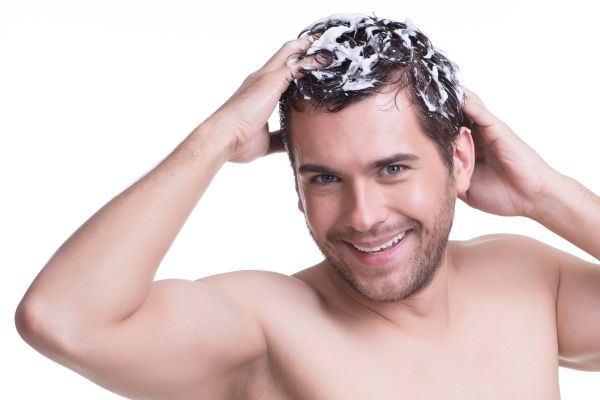 hombre blanco sonriente aplicando el champú a su cabello con ambas manos