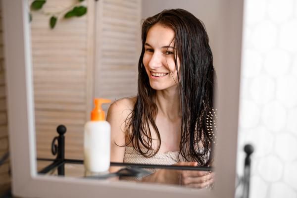 hidratar el pelo en casa - mujer joven delante del espejo cepillándose el cabello mojado