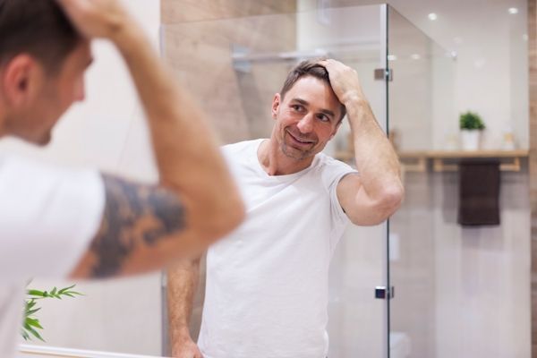 hidratar el pelo en casa - hombre sonriente con camiseta blanca pasándose la mano por la cabeza contento con su cabello
