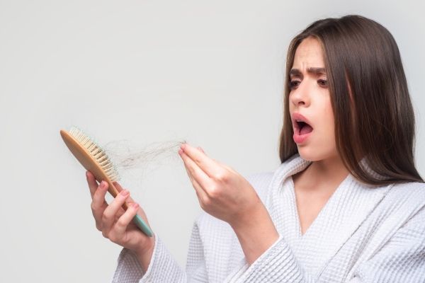 Mujer observando que pierde cabello de manera excesiva al peinarse, debido a un desajuste en la tiroides