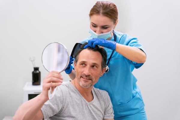 Cirujano capilar evaluando la evolución del implante de cabello en un paciente masculino, para asegurarse que todo marcha de manera adecuada