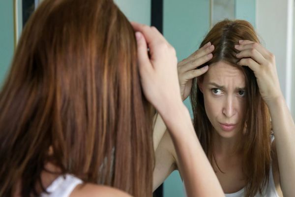 alopecia nerviosa - mujer mirándose en el espejo preocupada por el adelgazamiento de su cabello