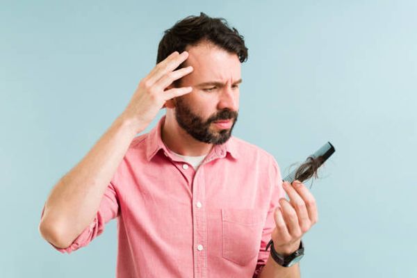 alopecia nerviosa - hombre con camisa rosa preocupado por el gran mechón de pelo que se ha quedado en el peine