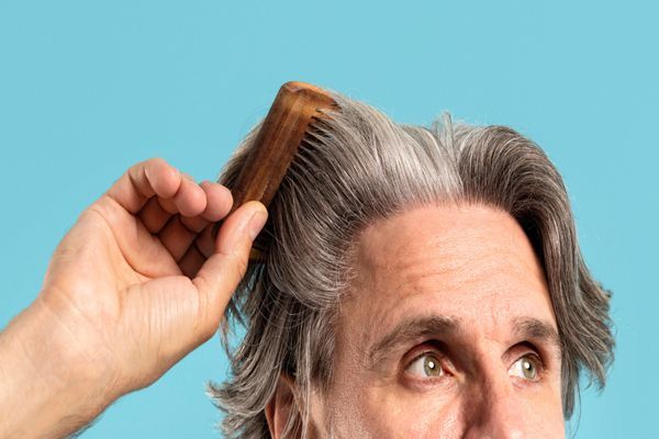 canas - hombre mayor con el pelo canoso peinando su melena con un cepillo de madera