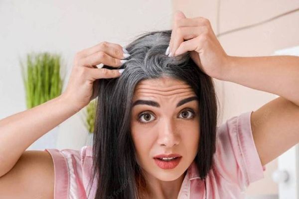 mujer revisando delante del espejo revisando los cabellos canosos de la cabeza
