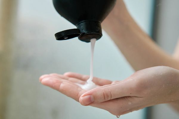 lavarse el cabello todos los días - mujer vertiendo un producto para el cuidado del pelo en su mano