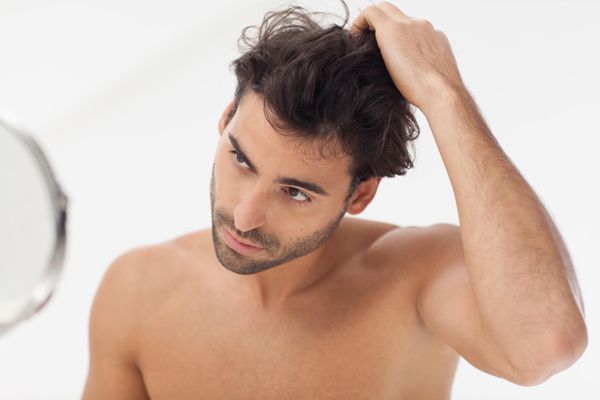 hombre pasando la mano por su pelo mientras revisa en el espejo el estado del mismo