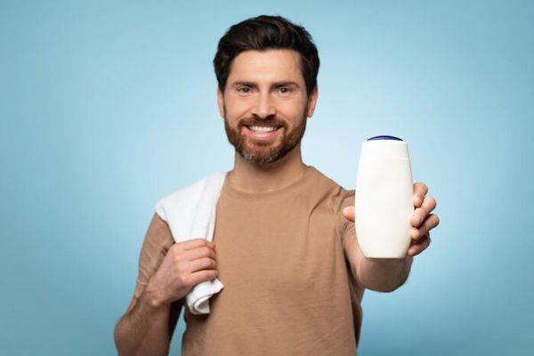 pica la cabeza - hombre adulto con camiseta mostrando un envase de champú sonriente