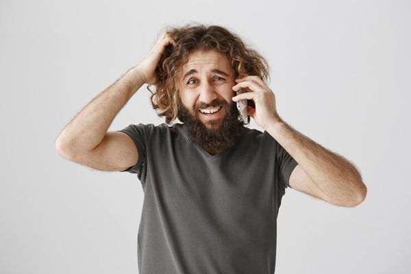 lavarse el cabello todos los días - hombre con el cabello rizado descuidado hablando por teléfono mientras se rasca la cabeza