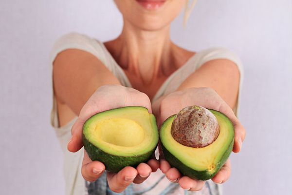 canas - mujer mostrando un aguacate partido en dos con una parte en cada mano