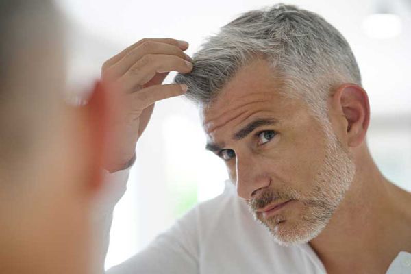canas - hombre revisando su cabello lleno de canas en el espejo del baño