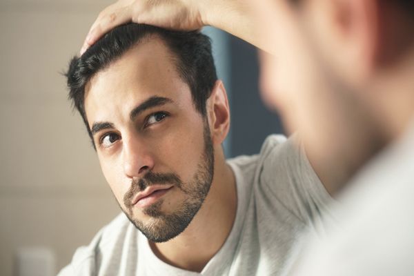 hombre en el espejo revisando el avance de las entradas de su cabello