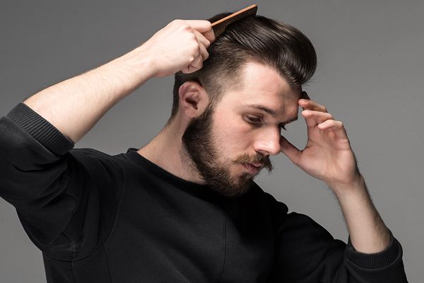 lavarse el cabello todos los días - hombre con una sudadera de manga larga negra pasando el peine por su tupe