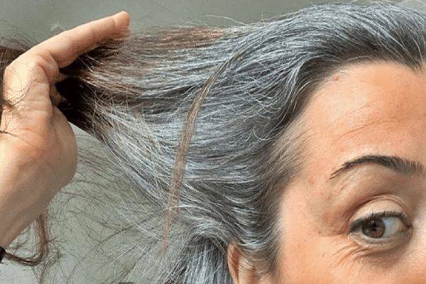 canas - mujer revisando su melena llena de canas mientras pasa la mano por el cabello
