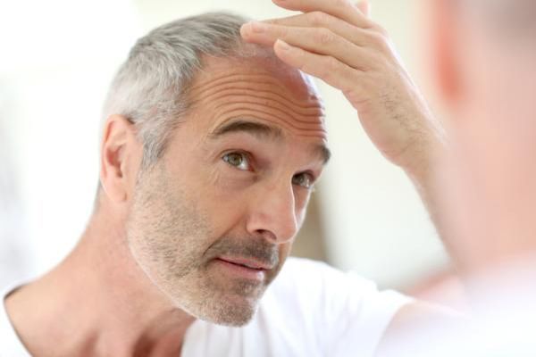 hombre con el pelo canoso delante del espejo revisando el retroceso de la línea del cabello
