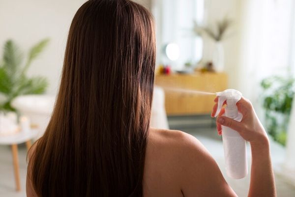 beneficios del vinagre para el cabello - mujer en el dormitorio aplicando vinagre en su cabello mediante un spray