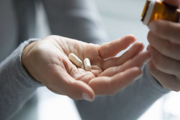 mujer con dos píldoras en la mano derecha y el bote de las píldoras en la mano izquierda
