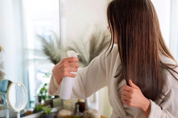 beneficios del vinagre para el cabello - mujer en el dormitorio aplicando vinagre en su cabello mediante un spray
