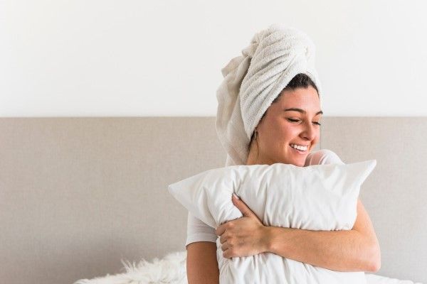 dormir con el pelo mojado - mujer en la cama abrazada a la almohada con una toalla cubriendo el cabello húmedo