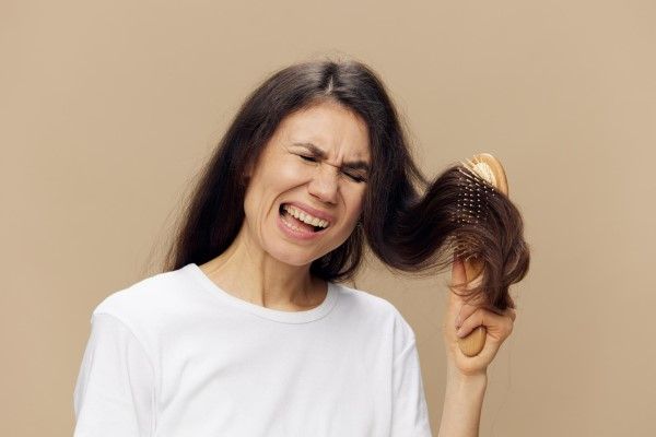mujer adulta con cara de sufrimiento al cepillar su cabello