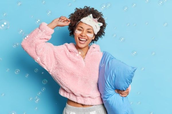dormir con el pelo mojado - mujer con ropa de dormir y una almohada en la mano muy contenta con montones de burbujas de jabón a su alrededor