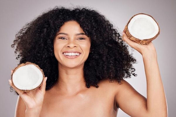 aceite de coco en el pelo - mujer sonriente con el cabello rizado y medio coco en cada mano