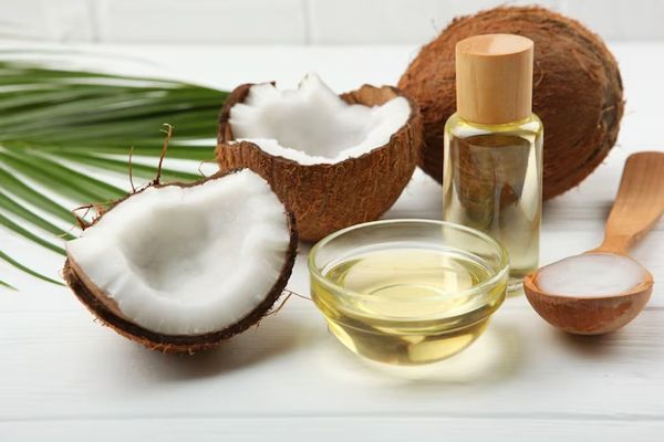 aceite de coco en el pelo - mesa con un coco entero y otro partido con una cucharada con agua de coco y un envase y un bol con aceite de coco