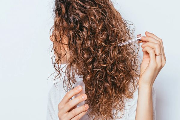 joven con el cabello rizado vertiendo el producto sobre su cabello