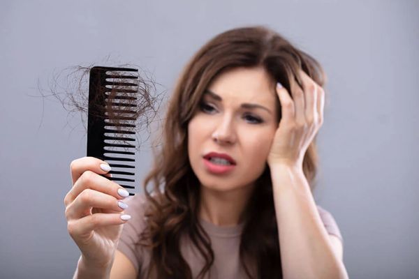 aceite de coco en el pelo - mujer llevándose la mano a la cabeza preocupada por el mechón de pelo que se ha quedado en el cepillo