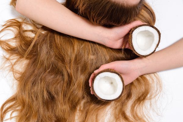aceite de coco en el pelo - imagen de la melena de una mujer tumbada con los dos brazos cruzados sobre el pelo con medico coco en cada mano