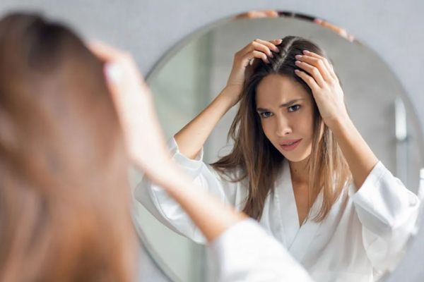 duele el cabello - mujer en pijama delante del espejo revisando su cabello con cara de sufrir molestias