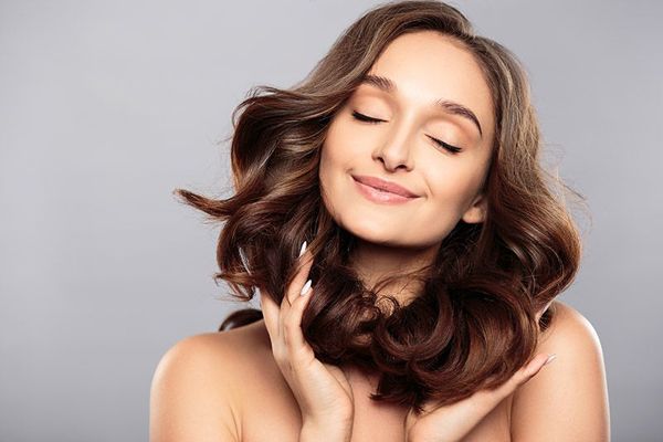 aceite de coco en el pelo - mujer sonriente acariciando su cabello con las manos