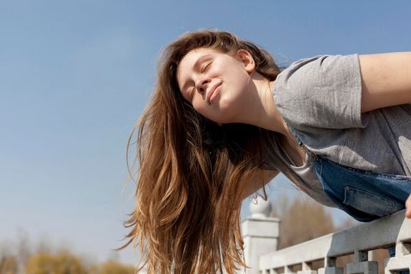 duele el cabello - mujer con el cabello largo y los ojos cerrados apoyada en una valla disfrutando del sol