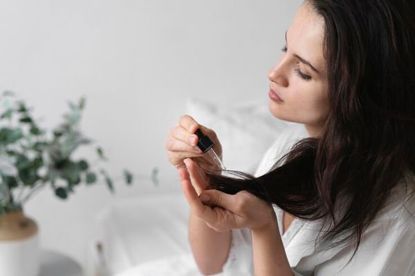 mujer sentada en la cama aplicando serum en la punta de su cabello