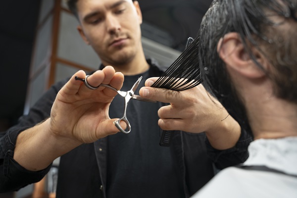 Barbero cortando el cabello de un cliente masculino, para eliminar las puntas abiertas y mantener una buena apariencia en su melena