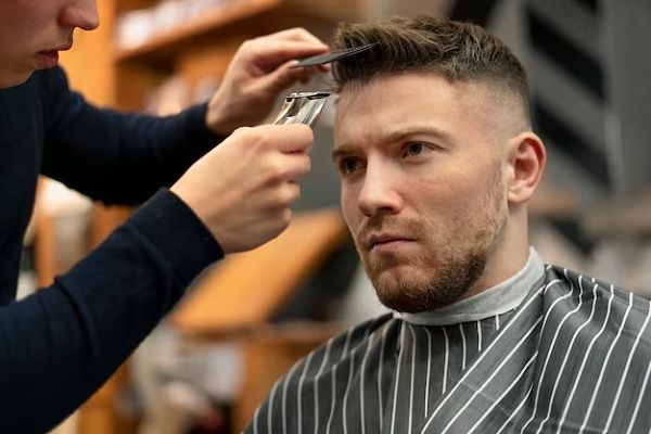 Cortes de pelo en el hombre según tu cara - Estilista realizando un corte de cabello a un hombre de acuerdo a la forma de su rostro, para resaltar los rasgos faciales y hacerlo lucir más atractivo
