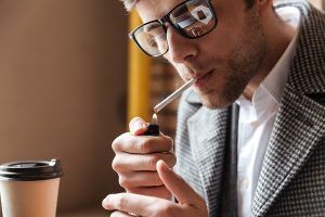 fumar aumenta la caída del pelo - hombre joven de traje encendiéndose un cigarrillo