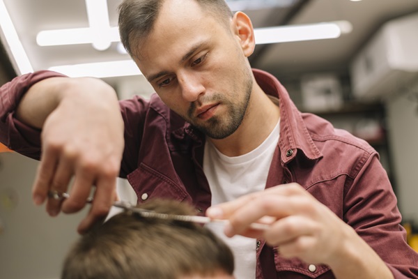 Barbaro cortando el cabello de un cliente masculino, para propiciar un crecimiento sano de las hebras capilares