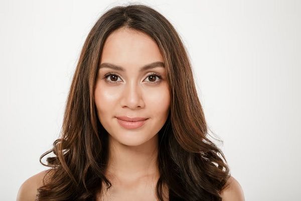 Femenina de rostro redondo con un cabello largo y en capas, el cual realza su belleza y rasgos faciales