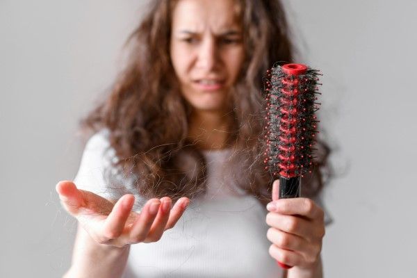 alopecia por tracción - mujer joven mirando con preocupación el cabello que se ha quedado en el cepillo tras el cepillado