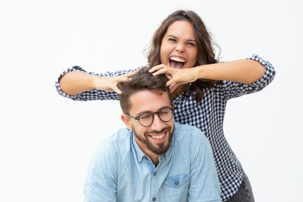 Cómo cuidar el pelo en los hombres - Joven con camisa de cuadros se muestra visiblemente sonriente mientras juega con el cabello de su pareja 