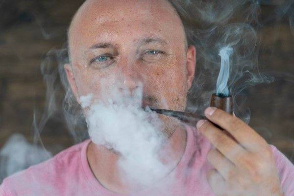 Fumar aumenta la caída del pelo - hombre adulto fumando en pipa rodeado por una gran cantidad de humo